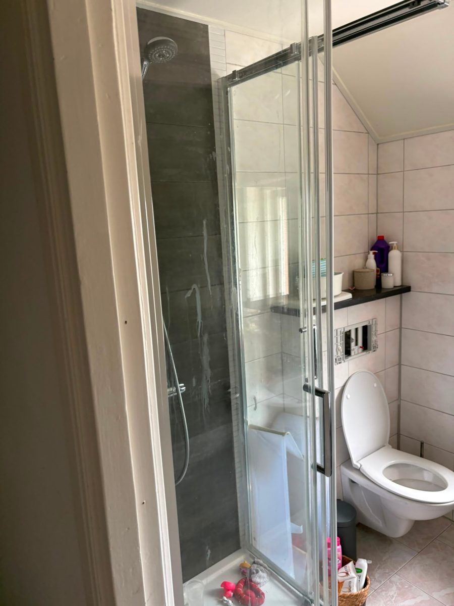 Oude douchecabine met witte tegels naast het toilet